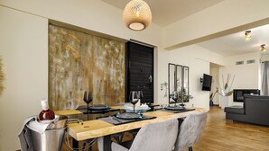 Ein Essbereich mit einem Holztisch, grauen Stühlen, einer Weinflasche und einem Fernseher im Hintergrund.