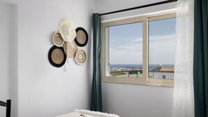 Ein Schlafzimmer mit einem Bett, einem Fenster mit Meerblick und einer Wand mit gewobenen Hüten.