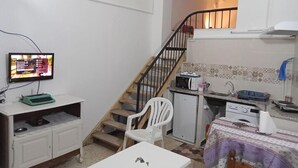 Ein kompakter Wohnbereich mit Küchenzeile, Essplatz, einem kleinen weißen Stuhl, einem Bett und einer Treppe.