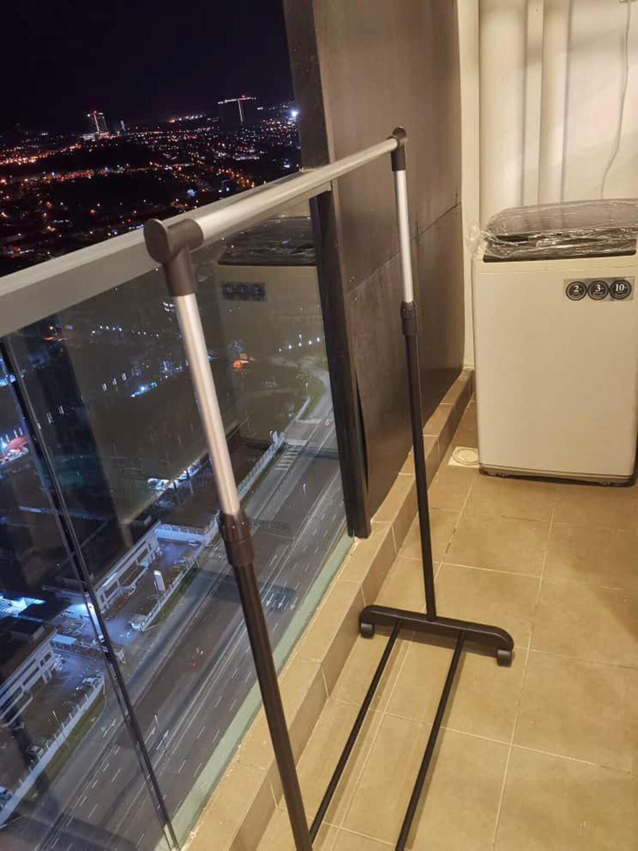 Un balcon doté d’une structure métallique, d’une rambarde en verre et offrant une vue sur le paysage urbain illuminé la nuit.