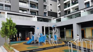 Ein Kinderspielplatz mit Rutschen und Klettergerüsten, umgeben von einem mehrstöckigen Gebäude mit Balkonen.