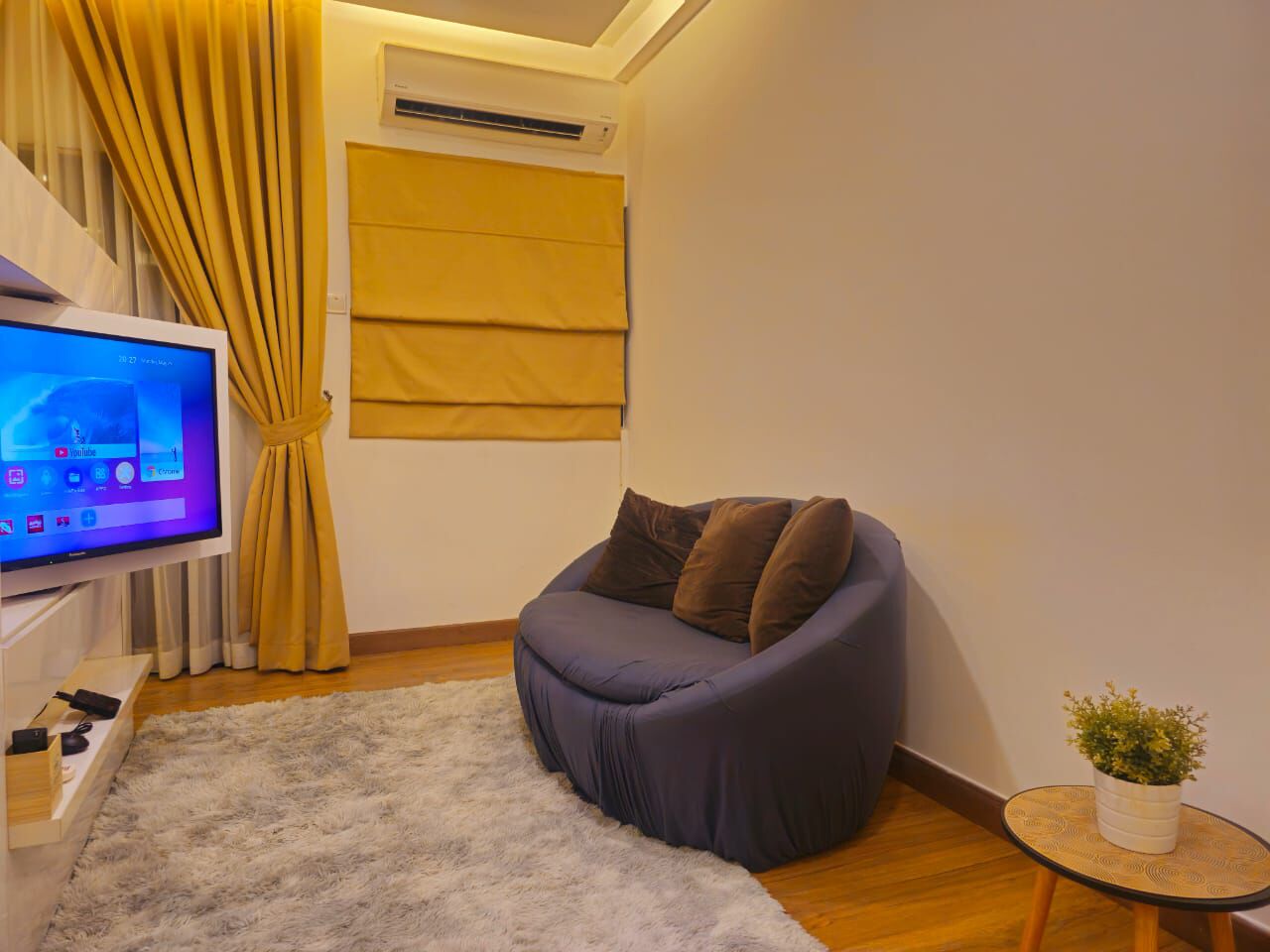 A modern living room with a sofa, a TV, a small table with a plant, and a window with curtains.