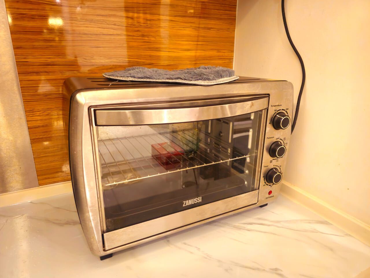 Horno tostador Zanussi con puerta de vidrio, perillas de control y cable de alimentación enchufado.