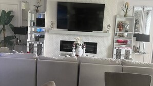 Ein modernes Wohnzimmer mit einem großen Flachbildfernseher, einem weißen Kamin und einem modularen Sofa.