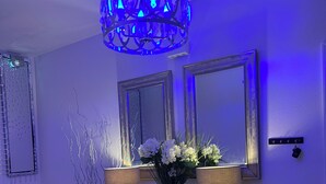 Ein modernes Interieur mit einem blauen Kronleuchter, zwei Wandspiegeln und einem Konsolentisch mit dekorativen Pflanzen und Lampen.