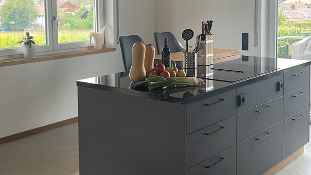 Et moderne køkken med en central ø, trælofter og store vinduer.