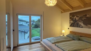 Et soveværelse med træloft, en seng med puder, et natbord med lampe og udsigt gennem en skydedør til et udendørs område.