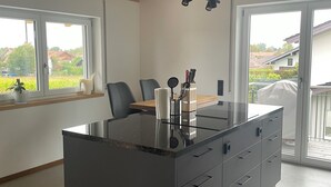 Et moderne køkken med en central ø, store vinduer og et træloft.