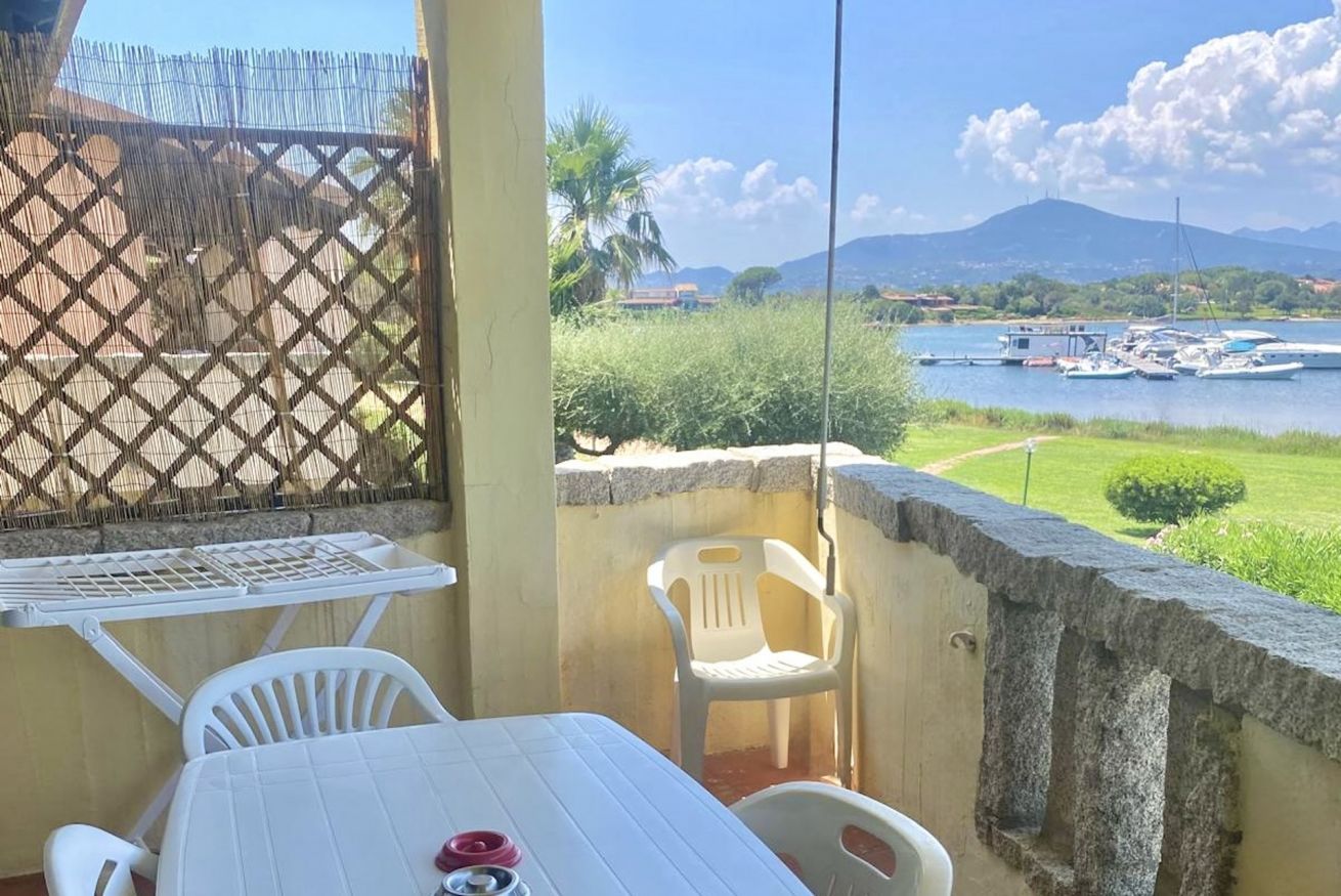 Un balcon avec une table et des chaises, une vue sur un lac où naviguent des bateaux et, au loin, une montagne.