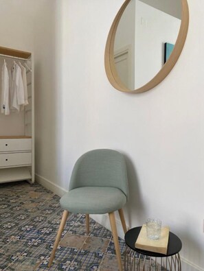 A room with a chair, a small table with a glass, a mirror on the wall, a wardrobe, and patterned floor tiles. - Palazzo Corselli b&b (Bagheria)