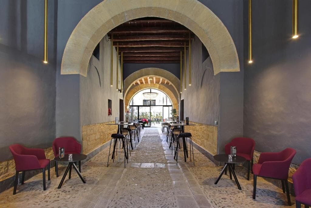 A corridor with tables and chairs, an arched ceiling, and a view through the arch.