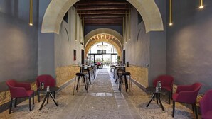 A corridor with tables and chairs, an arched ceiling, and a view through the arch.