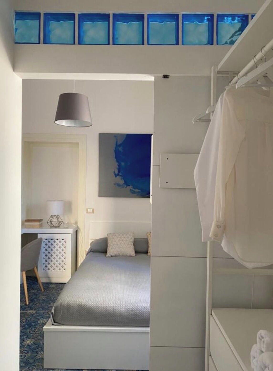 A bedroom with a bed, a desk, a chair, a hanging lamp, and a wall with abstract art.