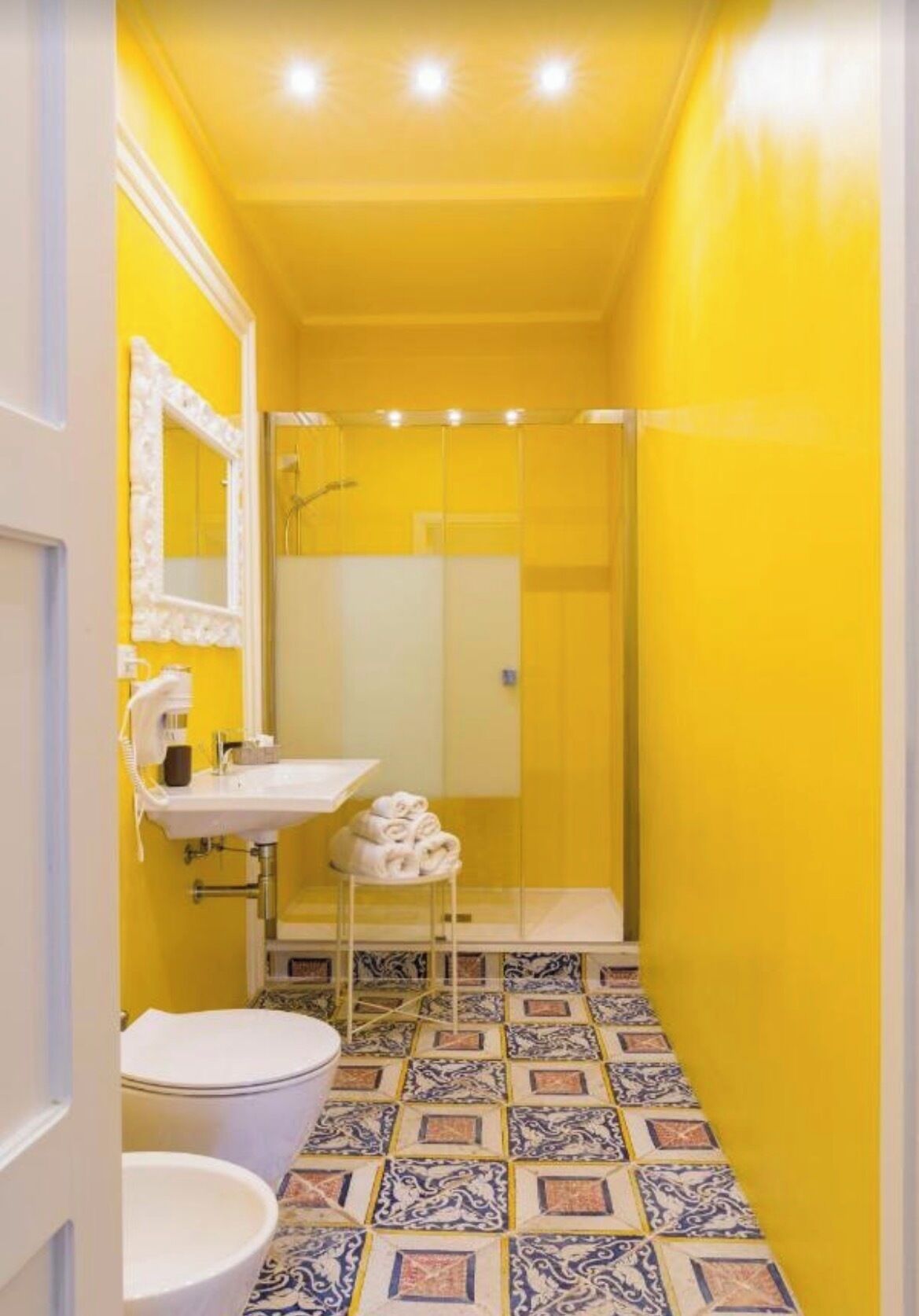 Un bagno con una parete gialla, un lavandino bianco, un water e una zona doccia.