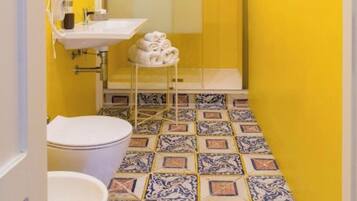 Un bagno con una parete gialla, un lavandino bianco, un water e una zona doccia.