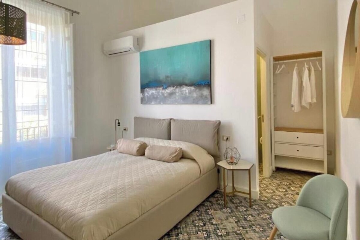 A bedroom with a bed, a bedside table, a chair, a wardrobe, and a painting on the wall.