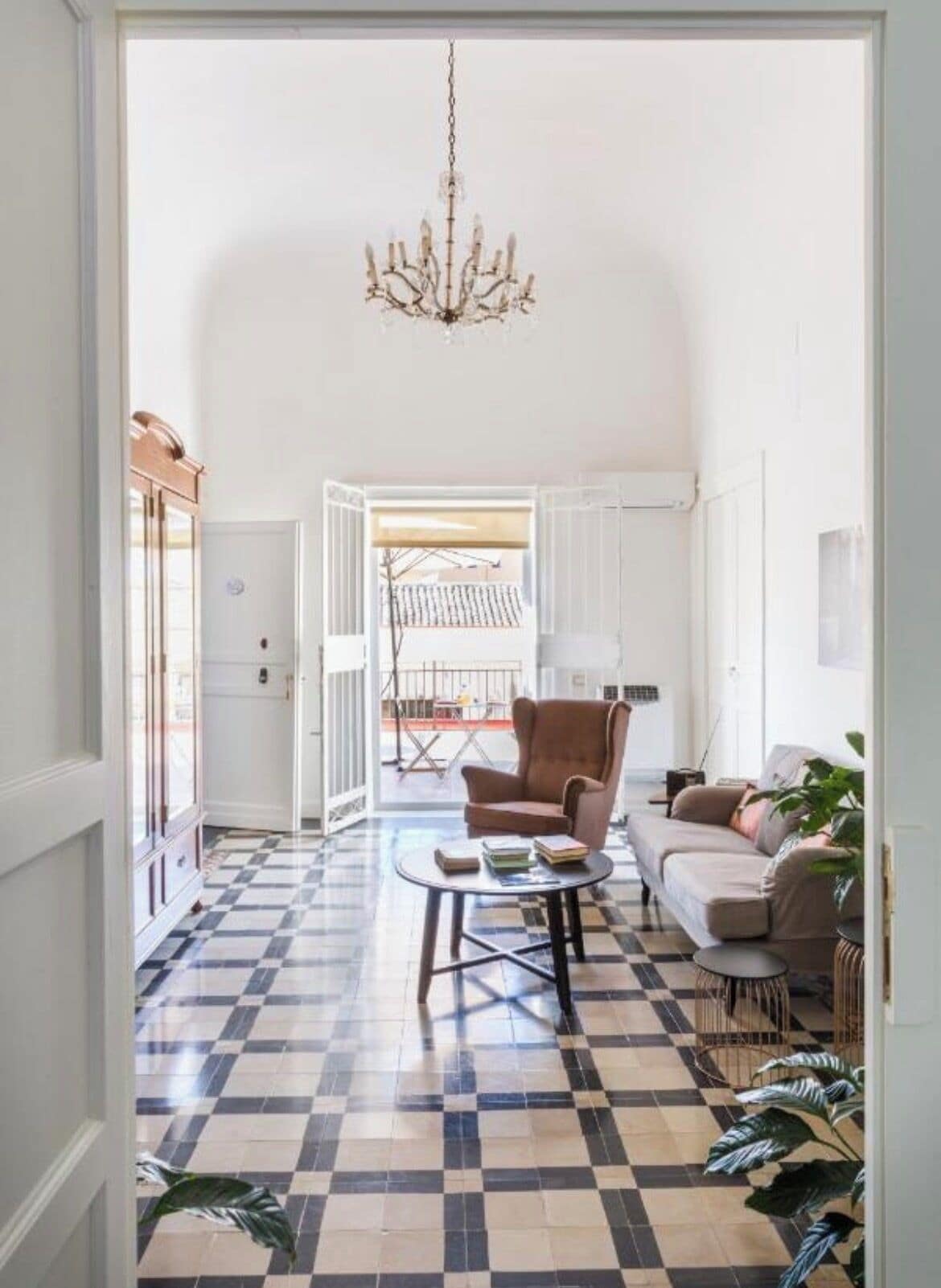 A living room with a checkered floor, a brown armchair, a sofa, a coffee table, and a chandelier.