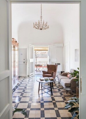 Un soggiorno con pavimento a scacchi, una poltrona marrone, un divano, un tavolino da caffè e un lampadario.