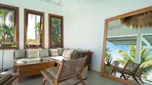 A room with a sofa, chairs, a table, and a large mirror reflecting the outdoors.