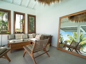 A room with a sofa, chairs, a table, and a large mirror reflecting the outdoors. - Villa Bananes Rouges (Trois-Rivières)