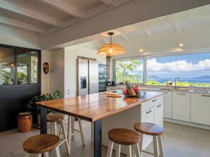A modern kitchen with a large island, bar stools, a hanging light fixture, and a view of the ocean. - Villa Bananes Rouges (Trois-Rivières)
