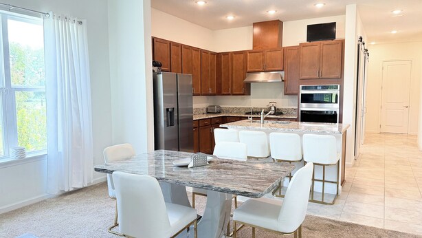 A modern kitchen with a marble island, white bar stools, stainless steel appliances, and wooden cabinets. - Cozy 2-bedroom cottage with AC in cool Jacksonville 55+ community in Mandarin (Jacksonville)