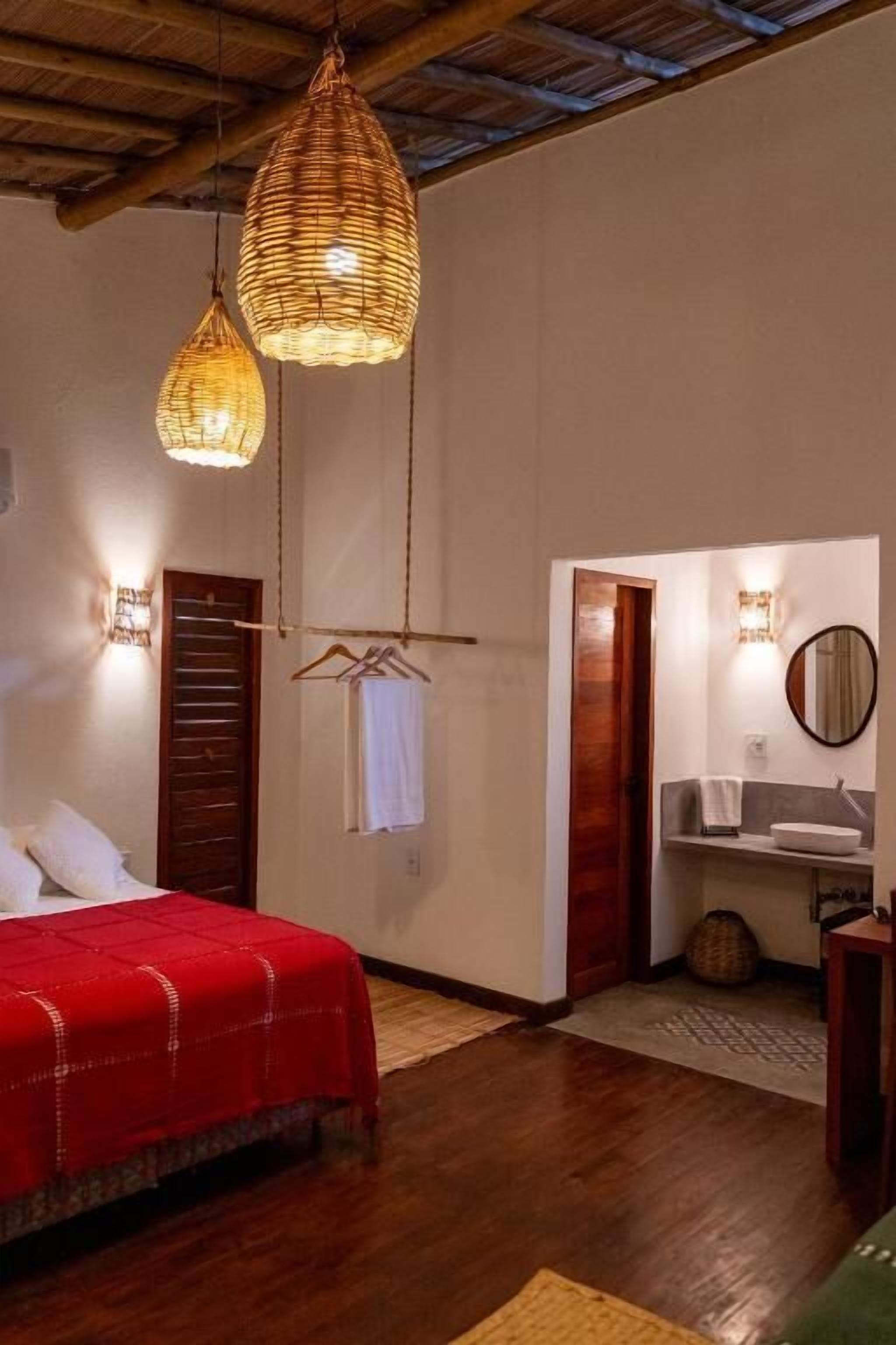 Un dormitorio con cama, lámpara colgante, puerta de madera y baño con lavabo y espejo.