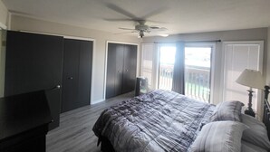 Une chambre à coucher comprenant un lit, un ventilateur de plafond, un bureau et une porte coulissante donnant sur un balcon.