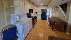 A compact kitchen with white cabinets, a black refrigerator, a wooden dining table, and a blue chair.