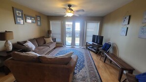 A living room with a sofa, a TV, a ceiling fan, and a large window.