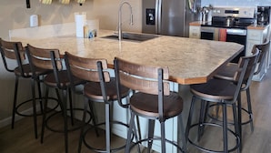 Una cocina moderna con una isla central, taburetes de bar, electrodomésticos de acero inoxidable y estantes de madera.