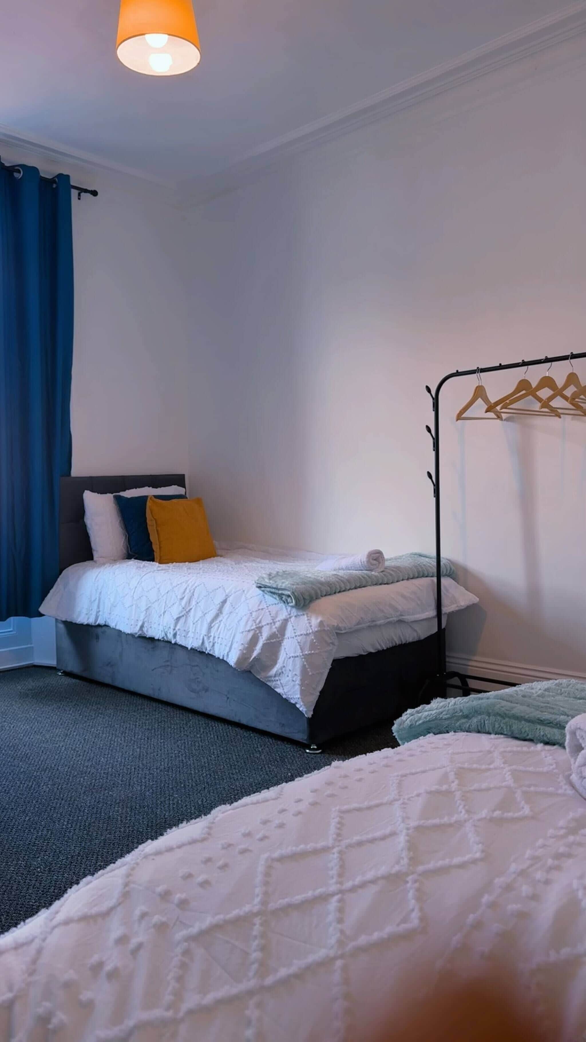 A bedroom with a bed, a bedside table, a hanging light fixture, and a window with curtains.