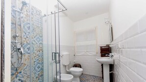 Casa de banho com chuveiro, sanita, lavatório e azulejos estampados.