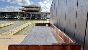 A wooden bench with a metal frame, a building with a green roof in the background, and a clear sky.