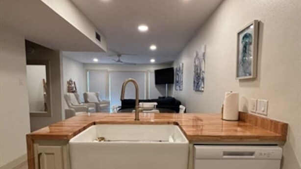 A kitchen with a wooden countertop, a built-in dishwasher, and a sink.