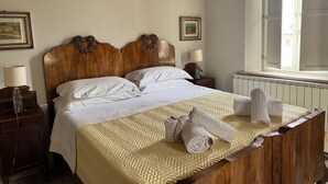 A hotel room with a wooden bed, white linens, a window with curtains, and a radiator. - Cozy Tuscan apartment near Siena, ideal for groups and families (Rosia)