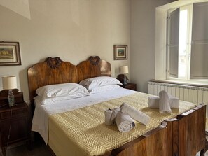 Ein Hotelzimmer mit einem hölzernen Bett, weißen Laken, einem Fenster mit Vorhängen und einer Heizung.