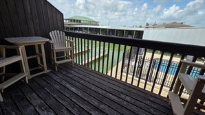 A wooden deck with a railing, two Adirondack chairs, and a view of a swimming pool.