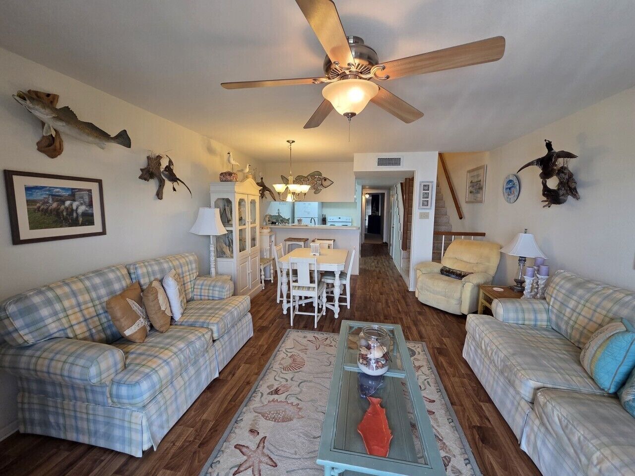 A living room with a ceiling fan, two sofas, a coffee table, and a dining area with a table and chairs.