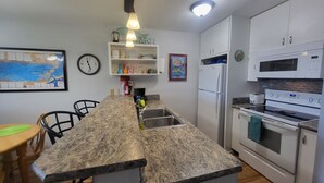 Une cuisine compacte dotée d’un plan de travail en granit, d’un four encastré, d’un réfrigérateur et d’un coin repas avec des chaises.
