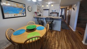 Un coin repas avec une table et des chaises en bois, une cuisine à l’arrière-plan et une carte accrochée au mur.