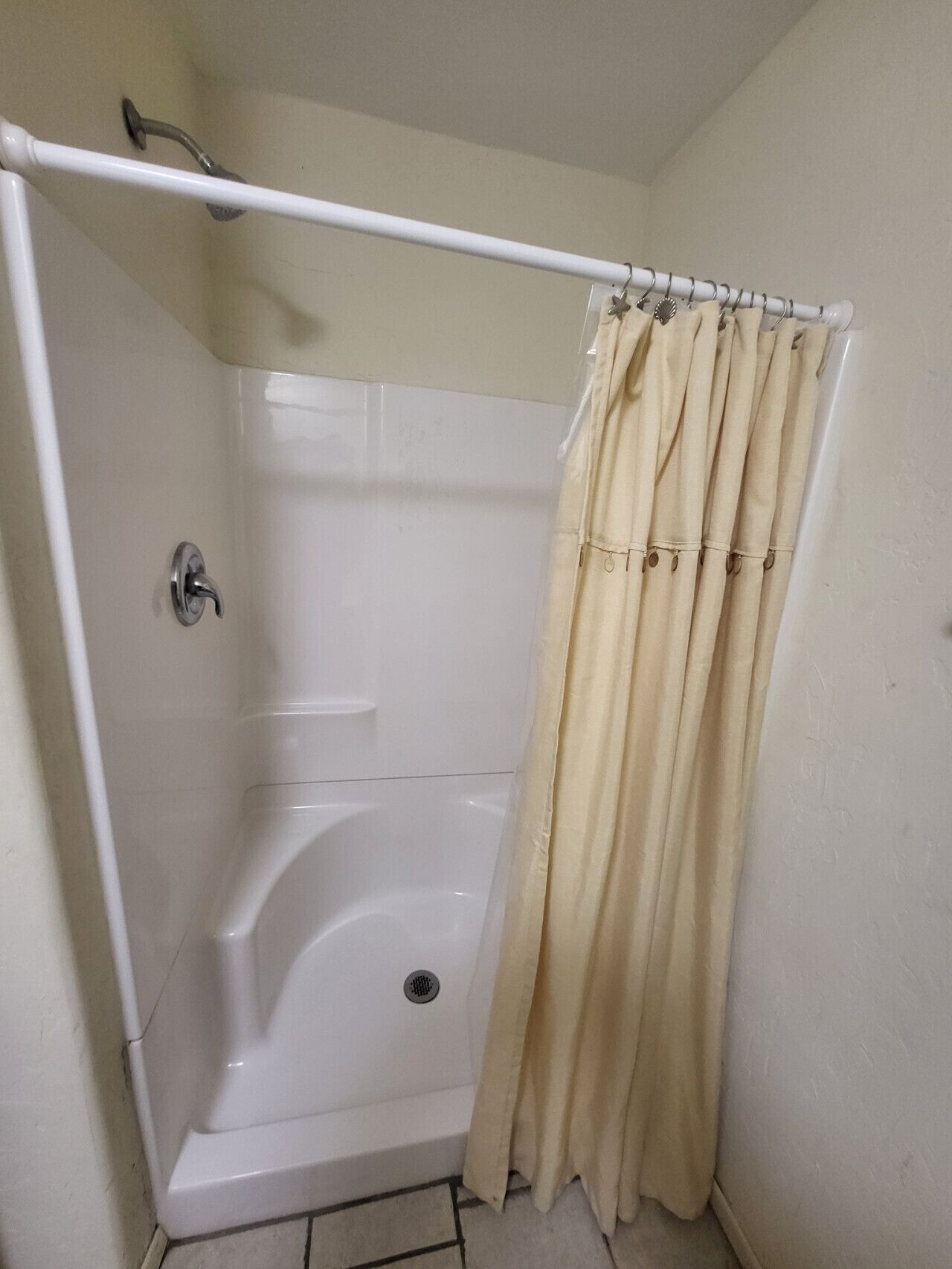 Ducha en esquina con bañera blanca, cortinas color crema y cabezal de ducha metálico.