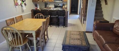 A dining area with a wooden table and chairs, a kitchen with wooden cabinets and appliances, and a brown leather sofa.
