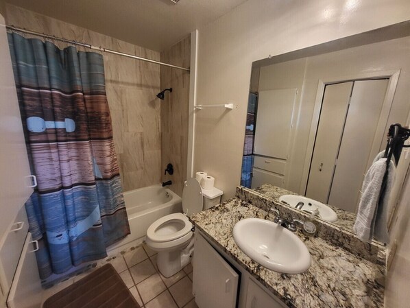 A bathroom with a shower curtain, toilet, sink, and mirror.
