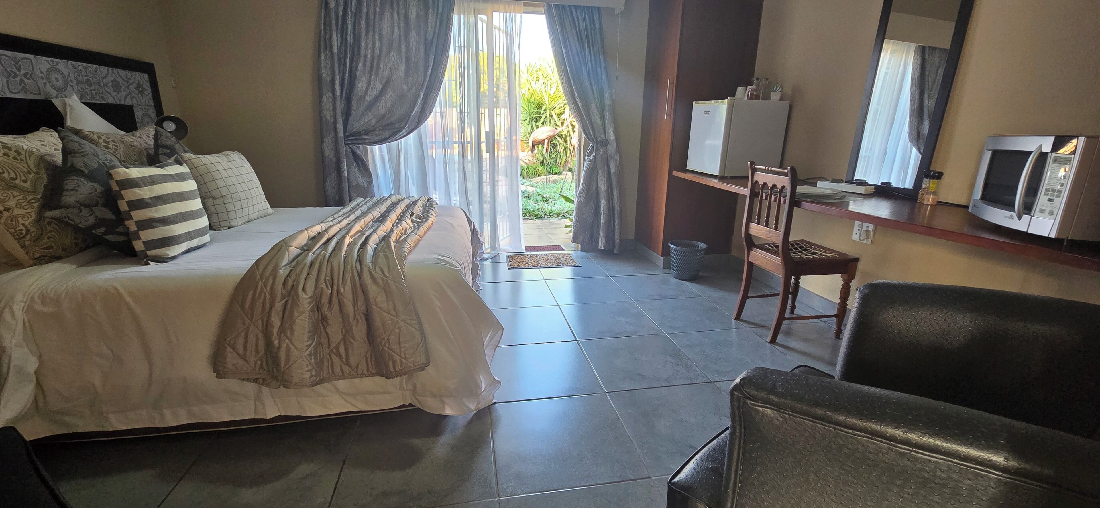 A hotel room with a bed, a desk, a chair, a microwave, and a refrigerator.