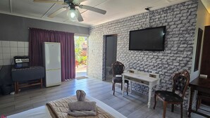 A modern room with a bed, a desk, a TV, and a kitchen area.