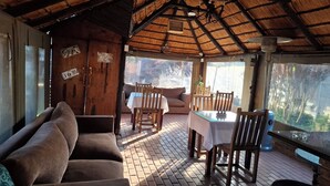 A covered outdoor seating area with a table and chairs, a sofa, and a wooden door with a sign.