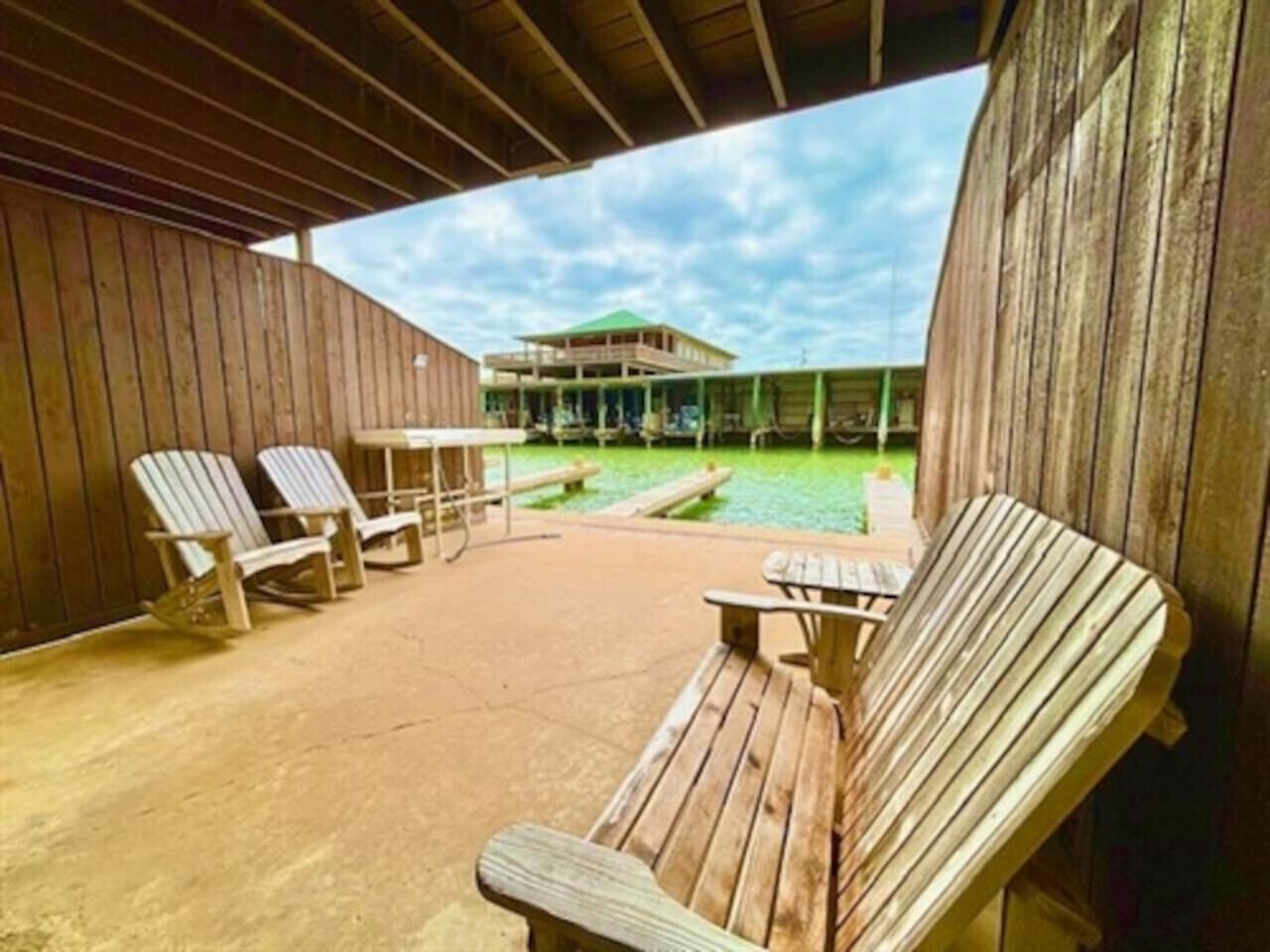 Un espacio al aire libre cubierto con bancos y sillas de madera, una mesa de picnic y vistas a un edificio con techo verde.