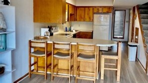 A kitchen with wooden cabinets, a central island with chairs, a refrigerator, and a ceiling fan. - Waterfront Condo with Private Boat Slip and Community Swimming Pool (Port O`Connor)
