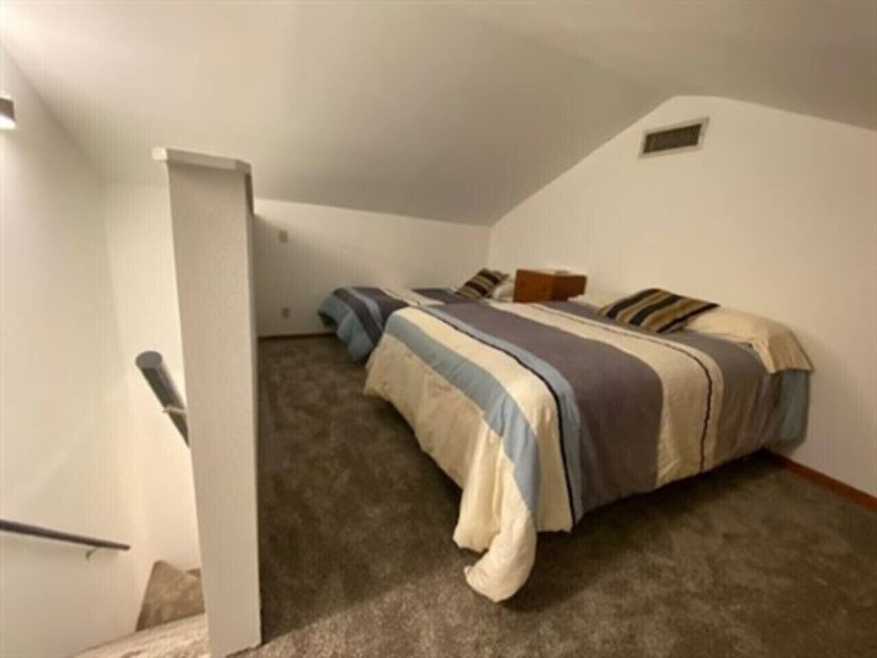 A bedroom with a bed, carpeted floor, and a door leading to another room.